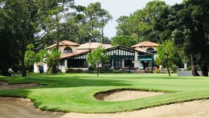 A golf course with a clubhouse featuring a Mediterranean architectural style, surrounded by lush greenery and trees. - "L'Etale", apartment with terrace in the heart of the city center. 2 steps from the lake (Soorts-Hossegor)