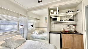 Une chambre de taille réduite comprenant un lit, un bureau, un four à micro-ondes et une petite kitchenette.