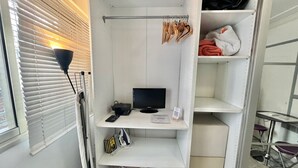 A compact room with a desk, a computer, and a shelving unit with clothes and bags. - Minerve 1,6 minuts walk from Palais (Cannes)