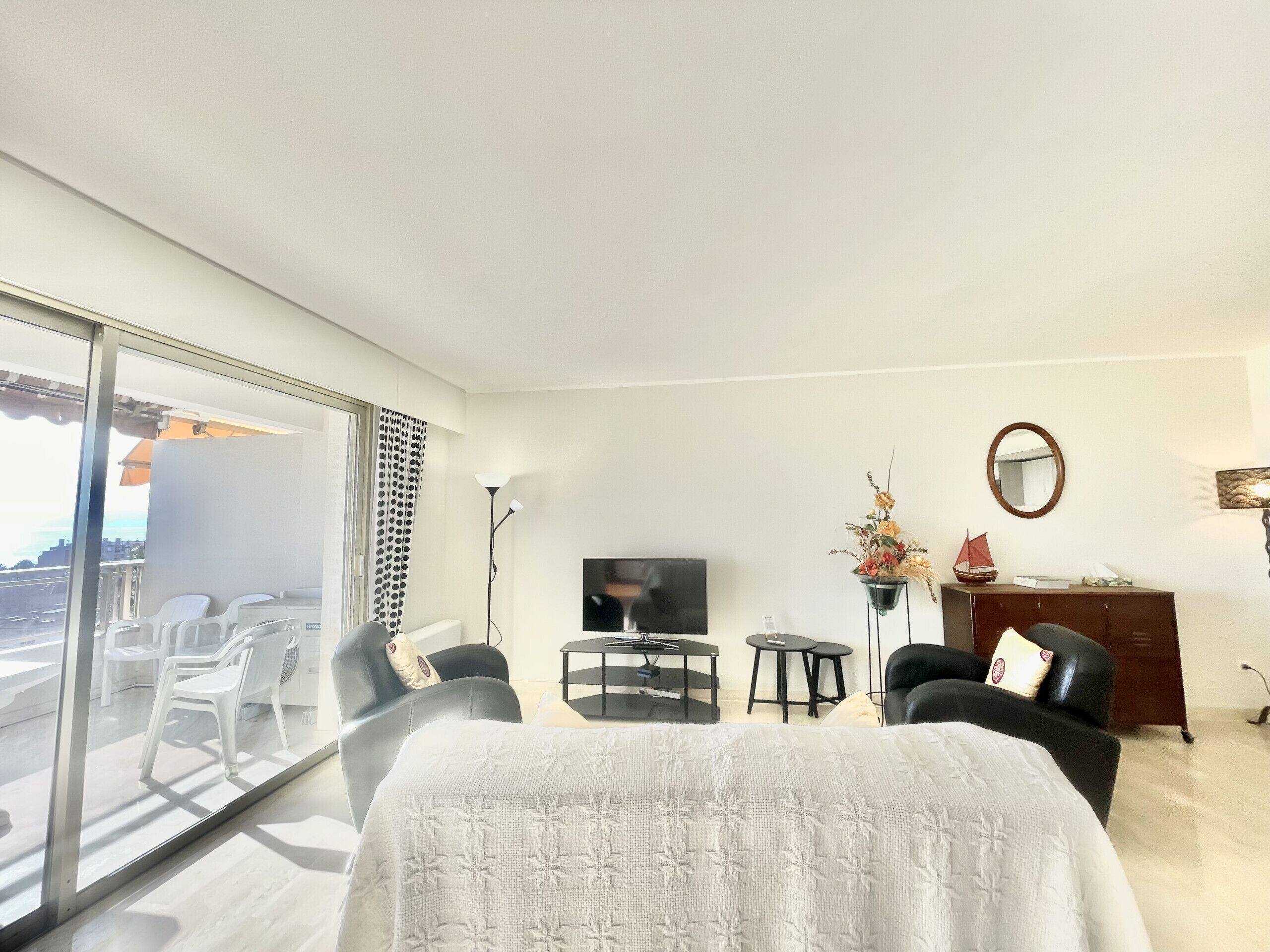 Een moderne woonkamer met een grote televisie, een bank, een eettafel en een balkon met stoelen.