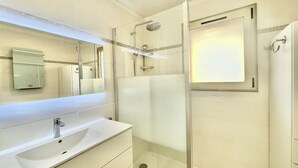 Une salle de bain moderne avec une douche à parois de verre, un grand miroir et un meuble-lavabo blanc.