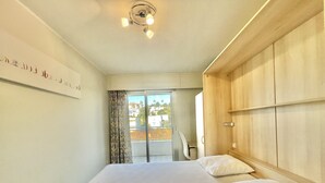 Une chambre avec un grand lit, une armoire en bois, un luminaire au plafond et une vue sur l’extérieur.