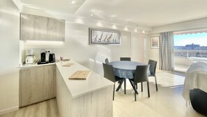 Une cuisine moderne dotée d’une machine à café intégrée, un coin repas avec une table ronde et des chaises, et une vue sur la ville grâce à de grandes fenêtres.