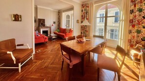 A living room with a wooden floor, a dining table with chairs, a red sofa, and a fireplace. - Novembre,10 minuts from Palais (Cannes)