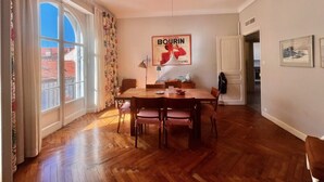 A dining area with a wooden table and chairs, a poster on the wall, and a window with curtains. - Novembre,10 minuts from Palais (Cannes)