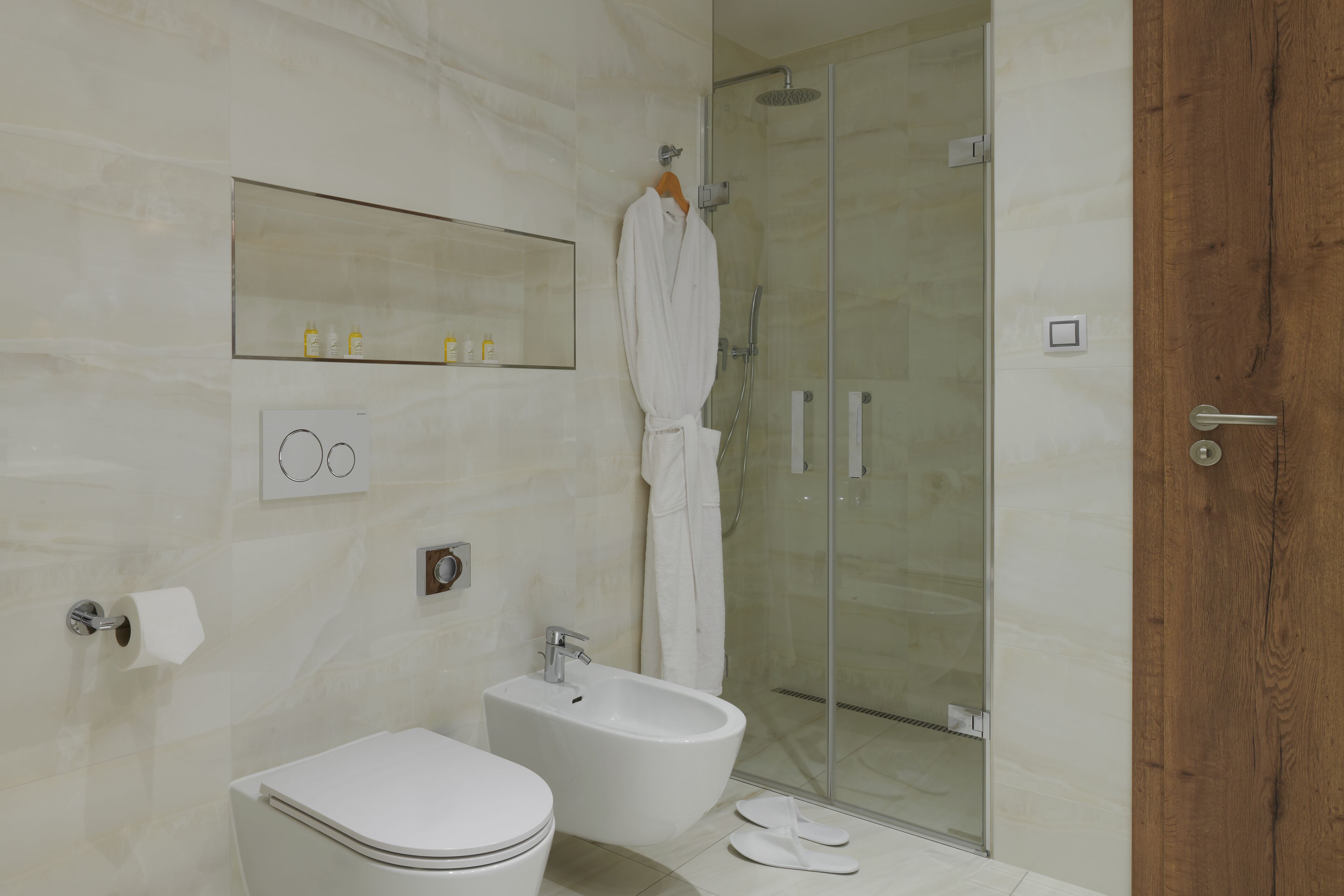 Uma casa de banho moderna com sanita, bidé e cabine de duche com parede de vidro.