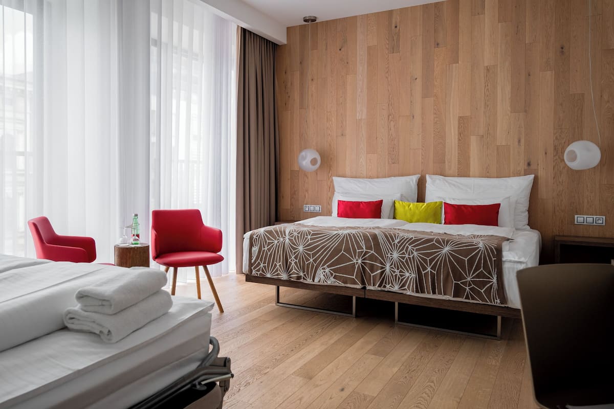 A hotel room with a large bed, a red armchair, a small side table, and a wooden headboard.