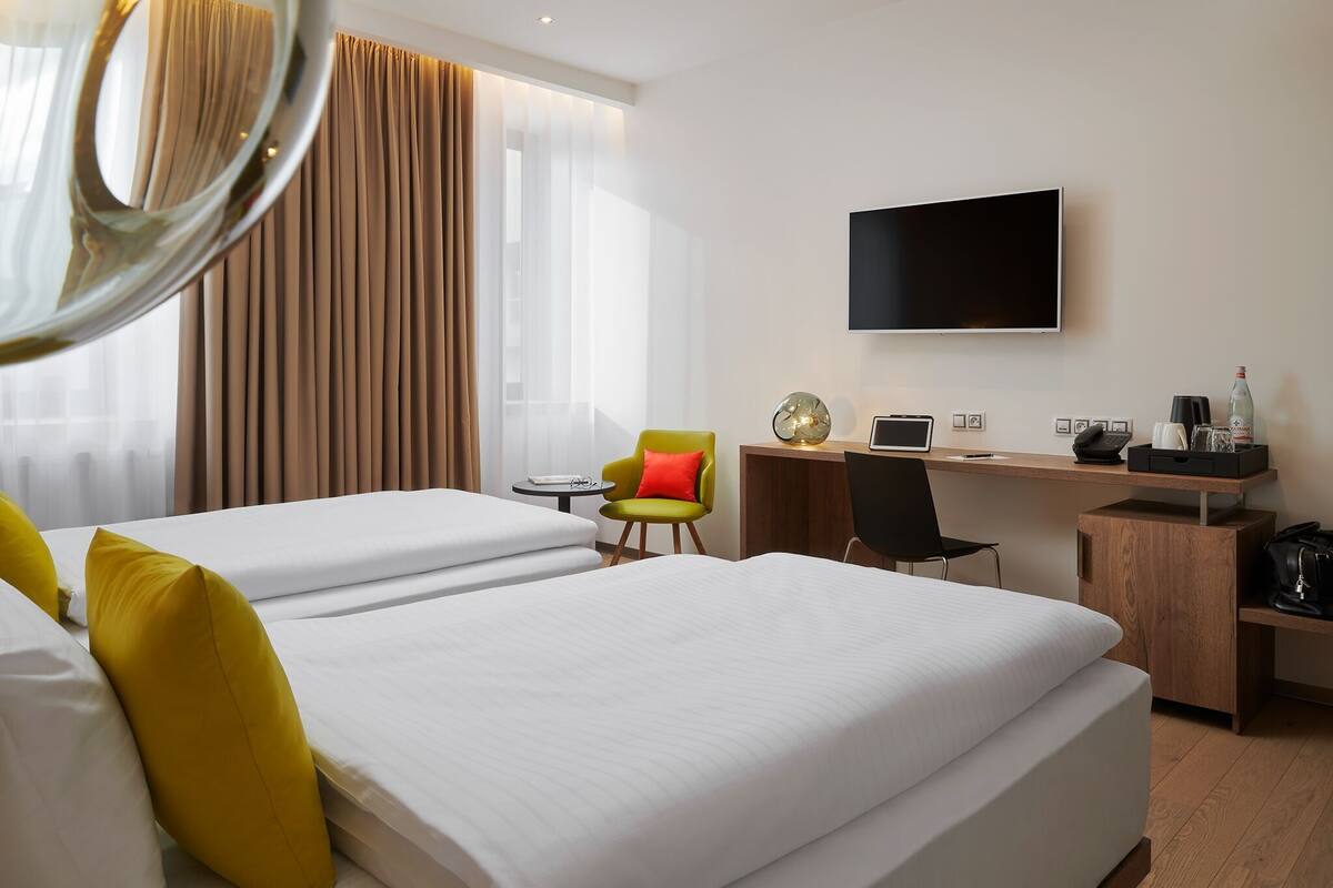 A hotel room with two beds, a desk with a computer, a TV, and a chair.
