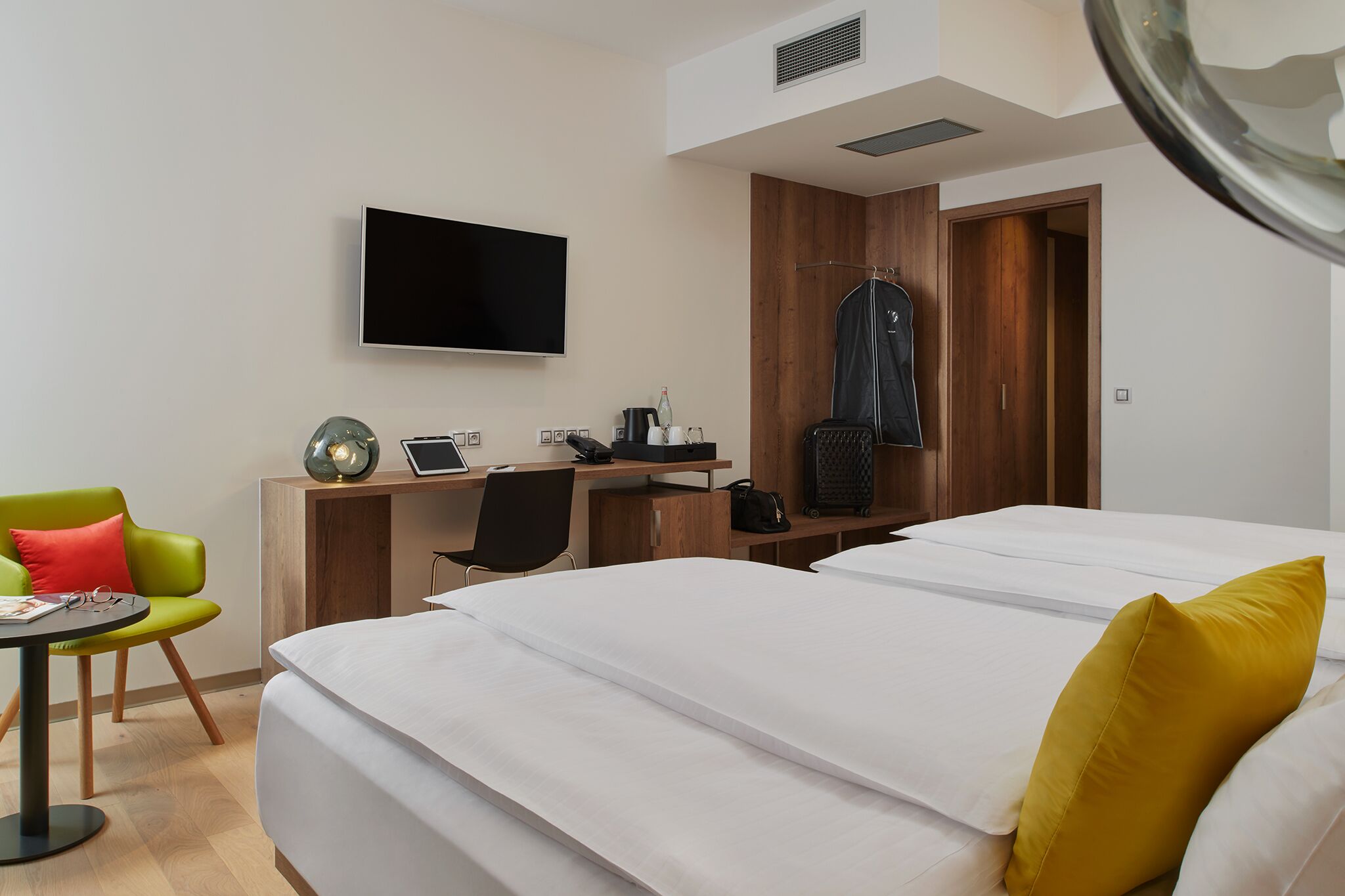 A hotel room with two beds, a desk with a computer, a TV, and a wardrobe.