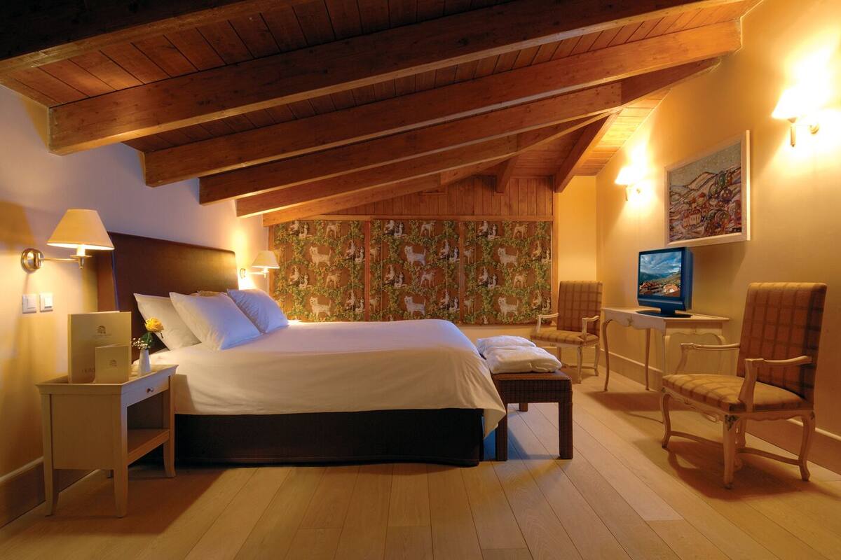 A bedroom with a large bed, a desk with a computer, a chair, and a wall with a patterned wallpaper.