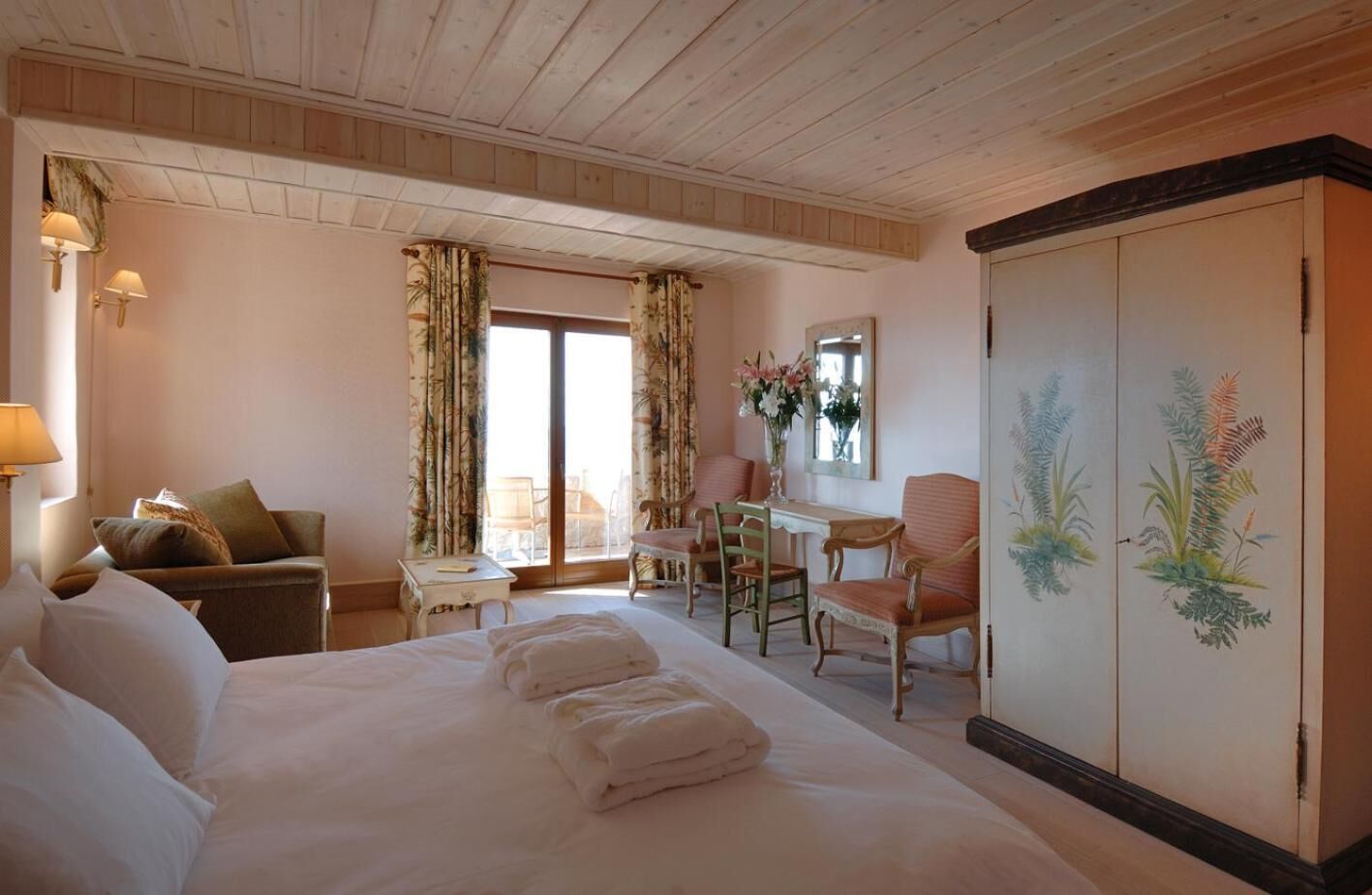 A hotel room with a large bed, a desk, a chair, a sofa, and a wardrobe.