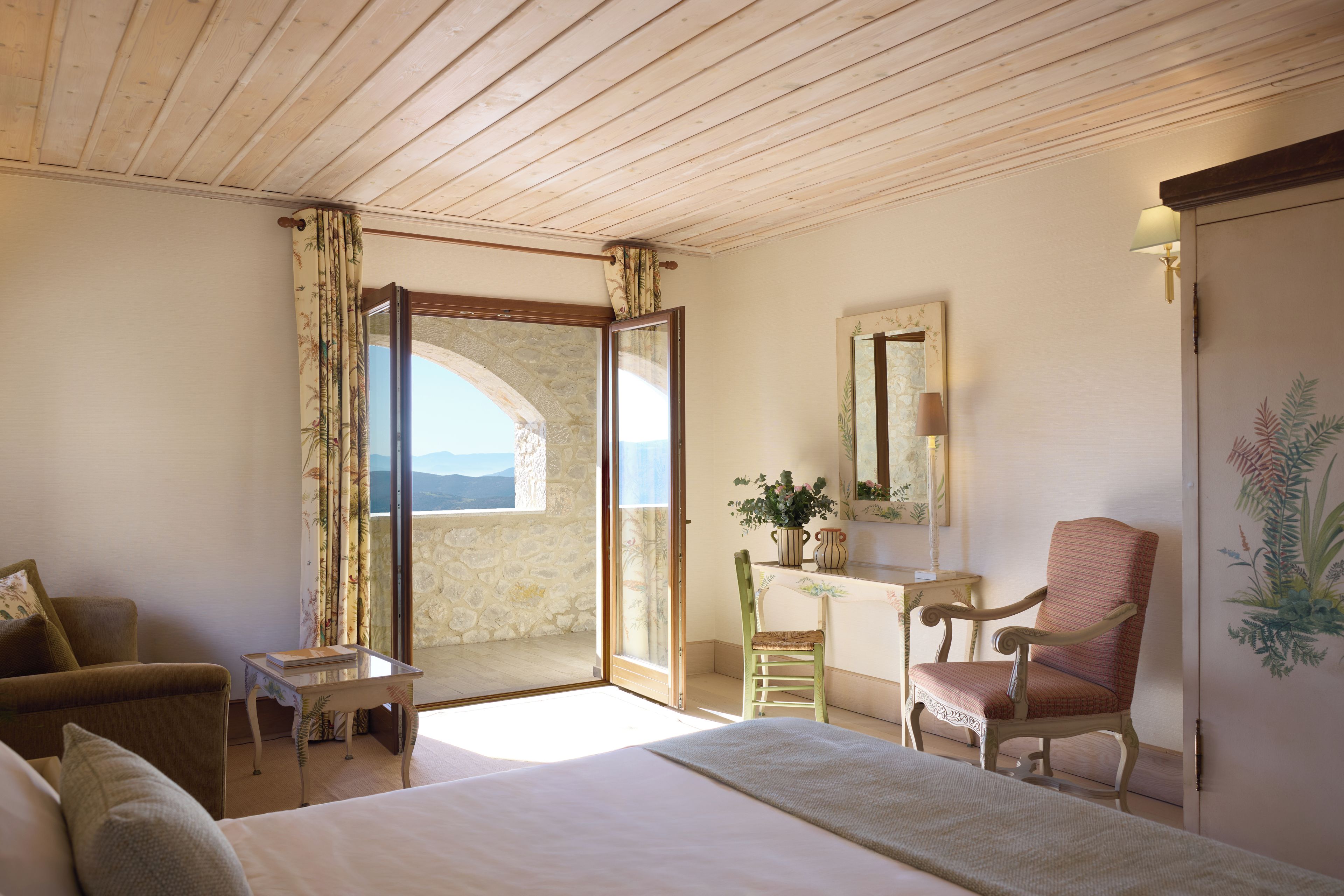 A room with a bed, a desk, a chair, and a view through an open door.