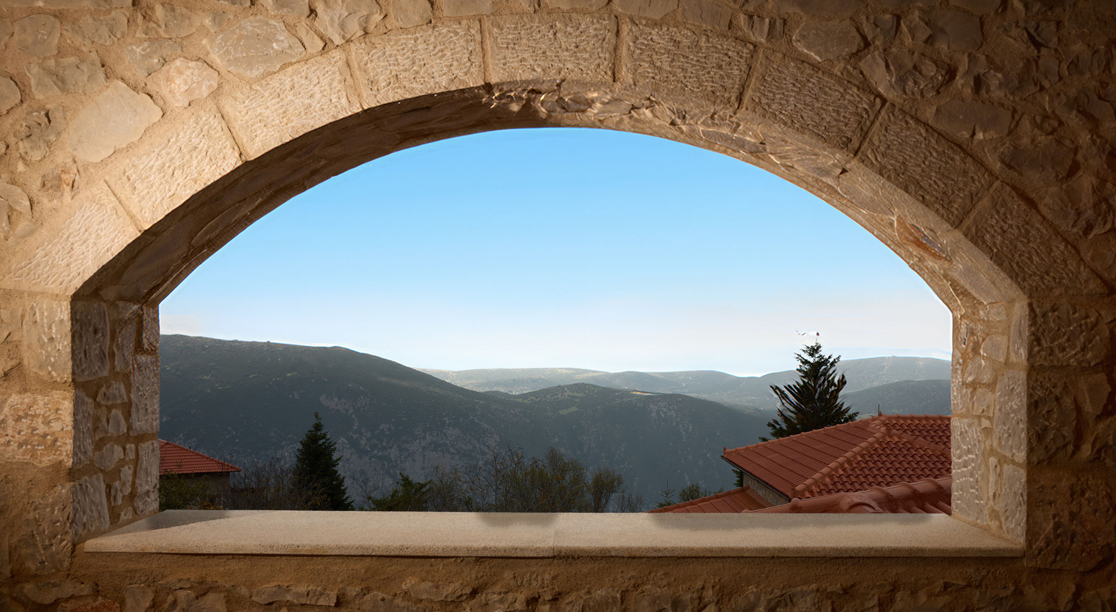 A stone arch window overlooking a mountainous landscape with a clear sky.