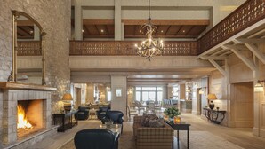 A spacious living area with a stone fireplace, a chandelier, and a high ceiling with wooden beams.