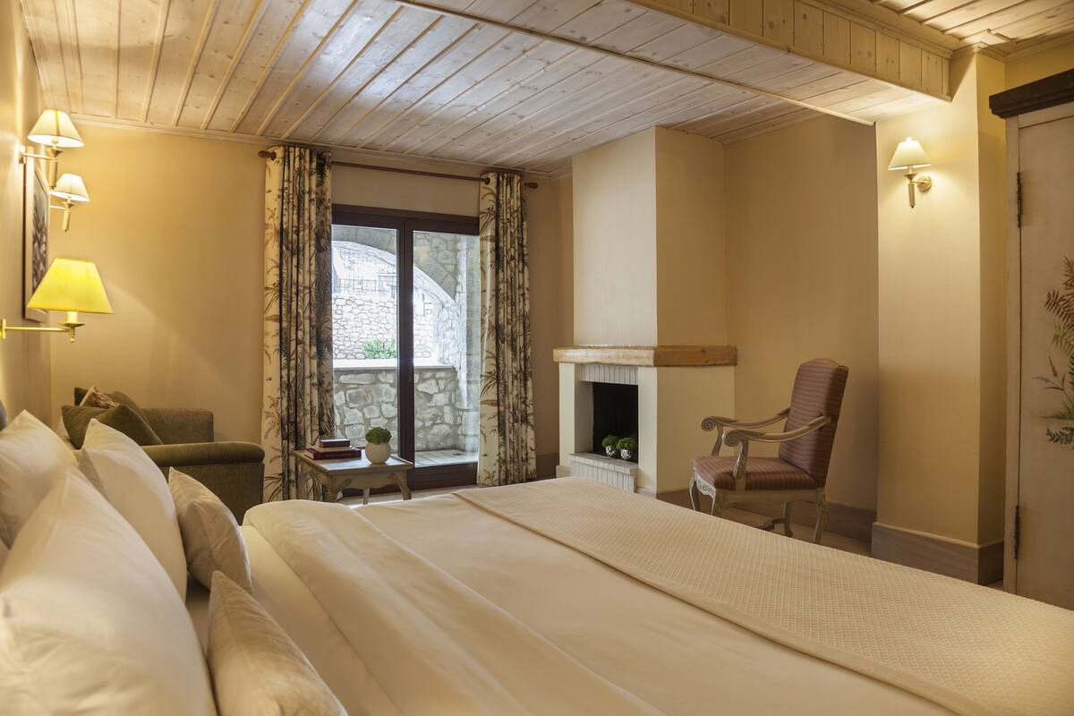 A bedroom with a bed, a chair, a fireplace, and a window with curtains.