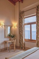 Habitación de hotel con escritorio de madera, una silla, un espejo y un ventanal con cortinas.