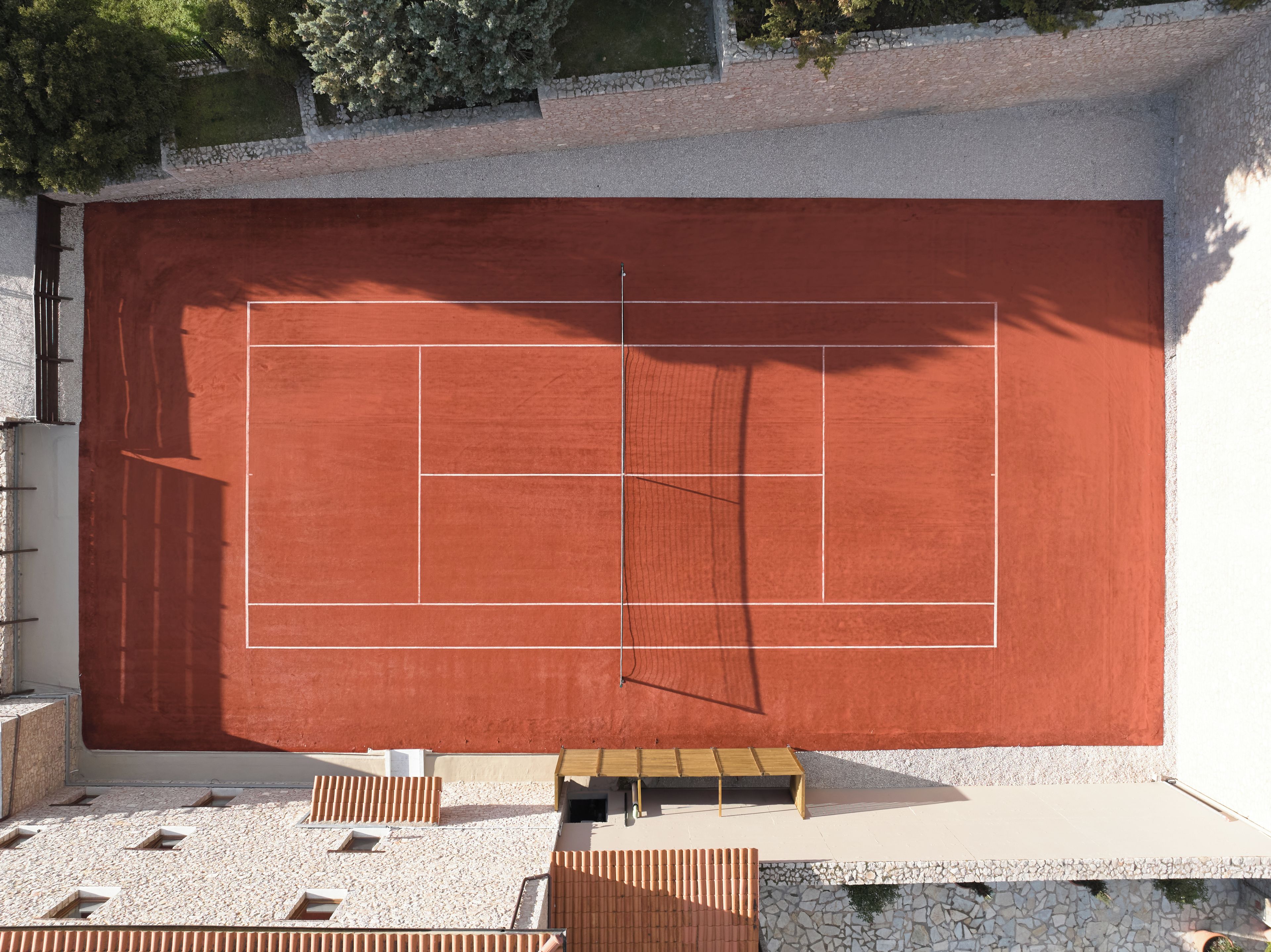 A tennis court with a net, surrounded by a stone wall and a wooden fence.