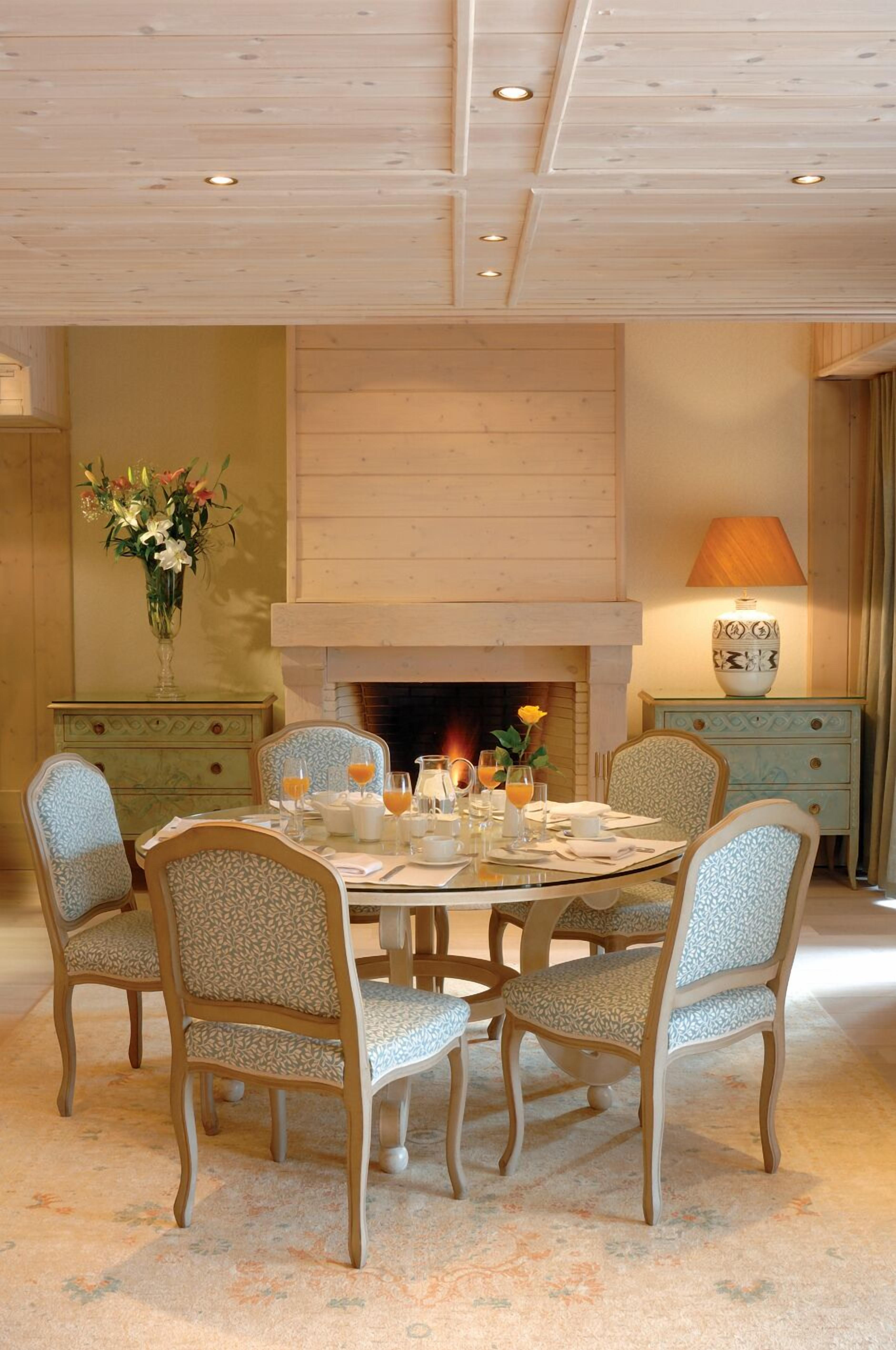 A dining room with a round table, six chairs, a fireplace, and a lamp.