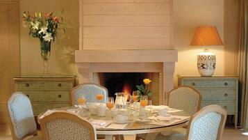 A dining room with a round table, six chairs, a fireplace, and a lamp.