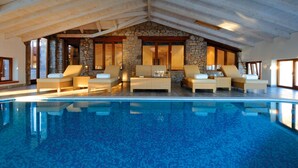 An indoor swimming pool with lounge chairs and a stone wall backdrop.