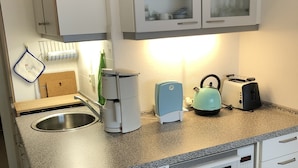 Eine kleine Küchenzeile mit Spüle, Kaffeemaschine, Toaster und Mikrowelle.