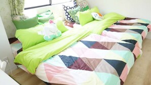 Uma cama com um edredom colorido, almofadas verdes e uma pequena estatueta de cachorro branco.