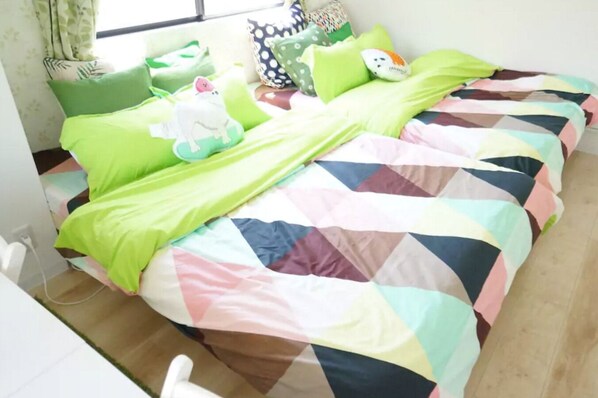 A bed with a colorful quilt, green pillows, and a small white dog figurine. - Not Ninja Kyocera Dome 1 - 4th Floor Room (Osaka)