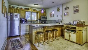 A kitchen with wooden cabinets, a refrigerator, a microwave, a sink, and a bar area with stools. - DF109- Centrally located in Canaan Valley! Pool! (Davis)