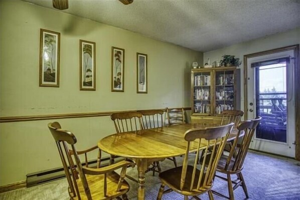 A dining room with a wooden table and chairs, framed pictures on the wall, and a bookshelf.