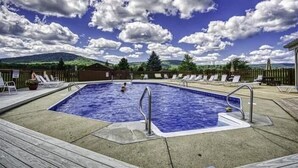 A swimming pool with a wooden deck, lounge chairs, and a view of a mountain range under a partly cloudy sky. - DF109- Centrally located in Canaan Valley! Pool! (Davis)