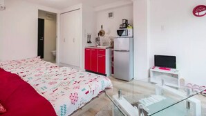 A bedroom with a bed, a red pillow, a kitchenette with a microwave, and a TV on a stand. - Not Ninja Kyocera Dome 1 - 5th Floor Room (Osaka)