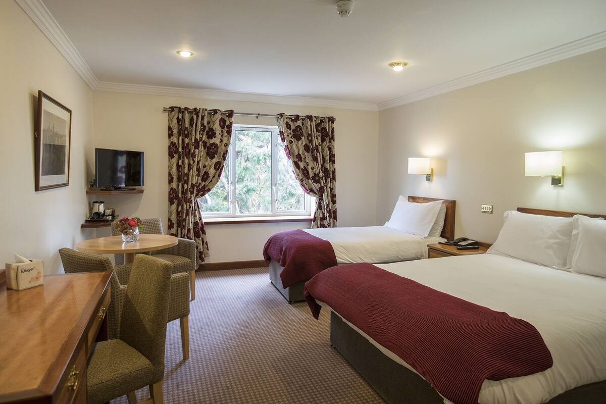A hotel room with two beds, a desk with a chair, a television, and a window with curtains.