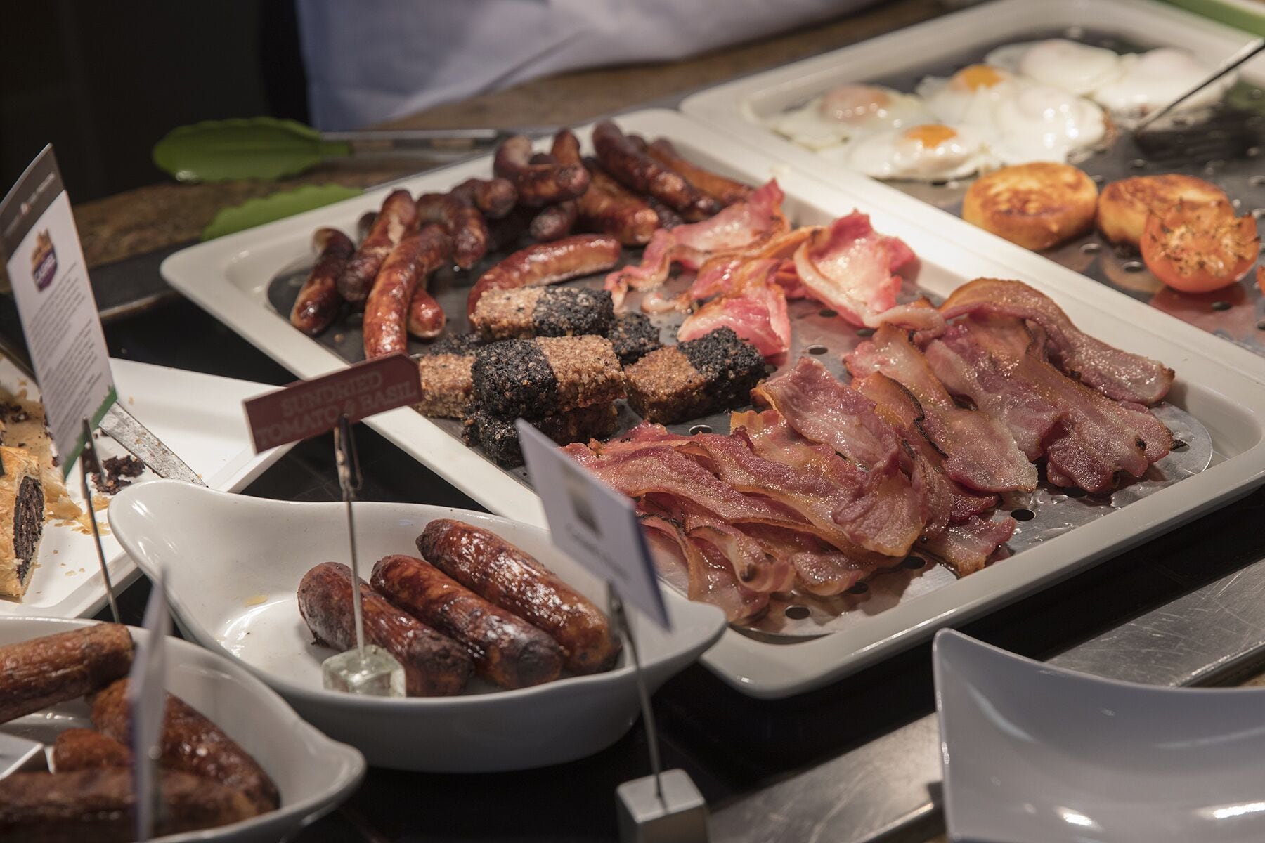 Un bufé con diversas opciones de desayuno, incluyendo salchichas, tocino, huevos y tostadas.