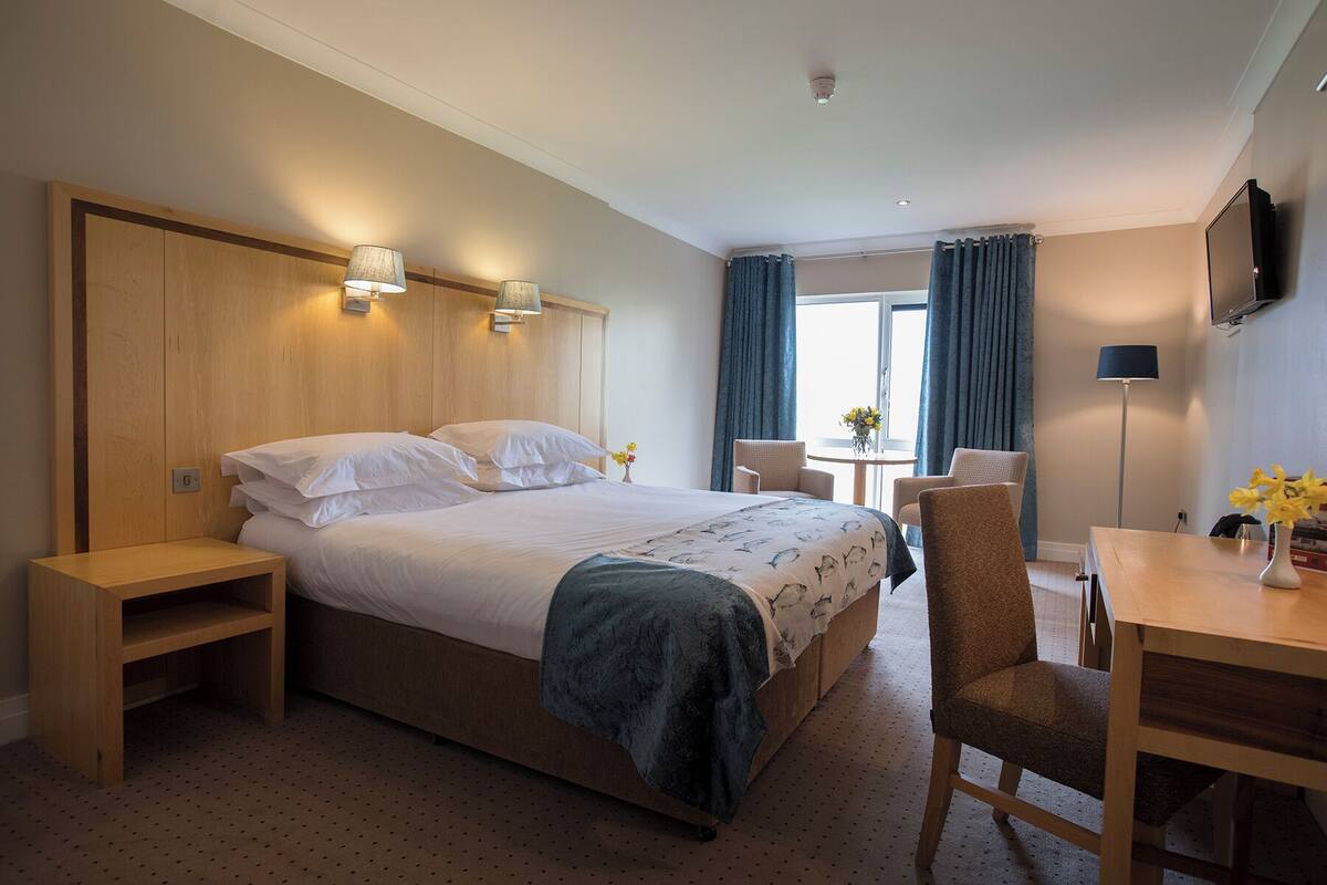 A hotel room with a large bed, bedside tables, a desk, and a chair.