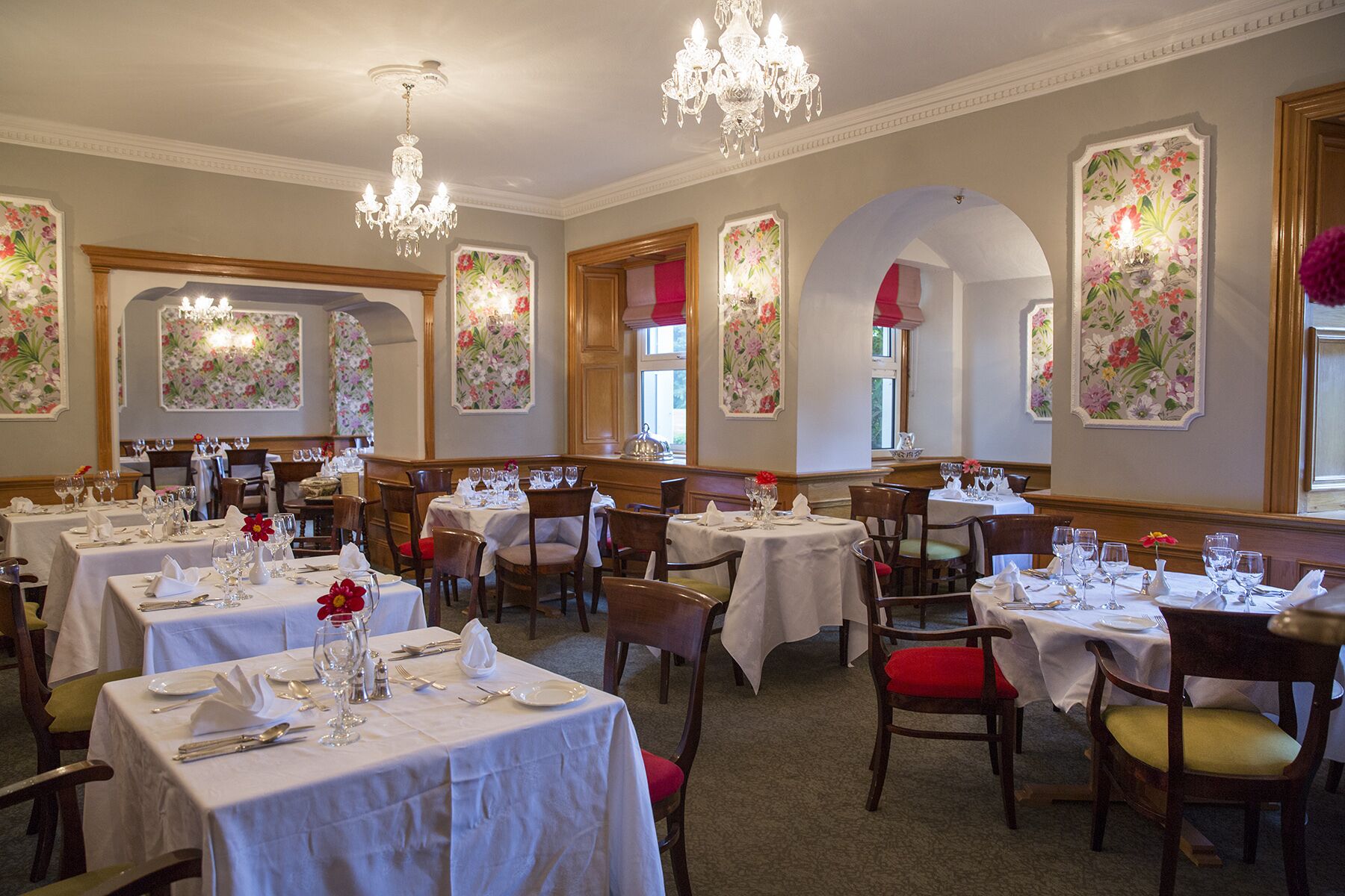 Une salle à manger avec plusieurs tables dressées, agrémentée de décorations florales murales et de lustres.