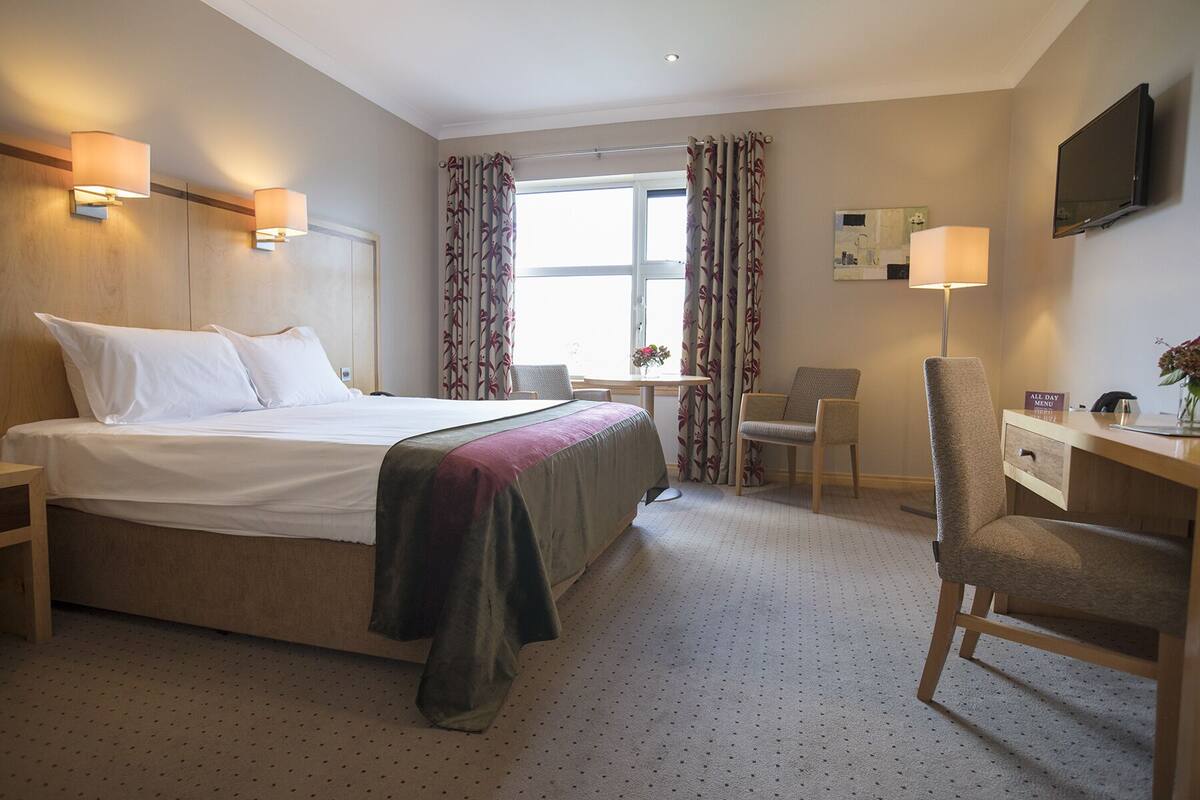 A hotel room with a bed, a desk, a chair, a TV, and a window with curtains.