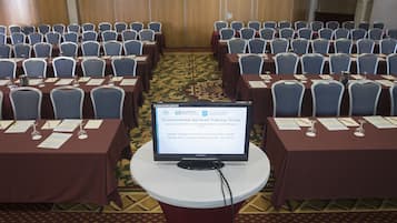 Un salón de conferencias con filas de mesas y sillas, una pantalla mostrando información sobre un grupo de capacitación en servicios ambientales, y piso alfombrado.
