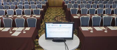 A conference room with rows of tables and chairs, a screen displaying information about an environmental services training group, and a carpeted floor.