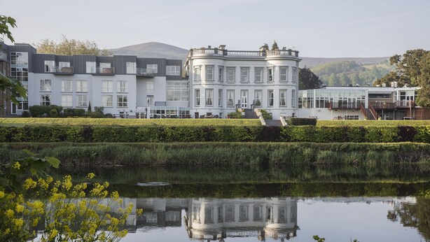 A large, historic building with multiple windows and a central entrance, surrounded by a well-maintained garden and a calm pond. - Hotel Minella (Clonmel)