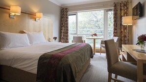 A hotel room with a large bed, a desk, and a chair. There is a window with curtains, a small table with a vase of flowers, and a television mounted on the wall. - Hotel Minella (Clonmel)