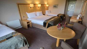 A hotel room with two beds, a small table with a vase of flowers, and a seating area with a sofa and armchairs.