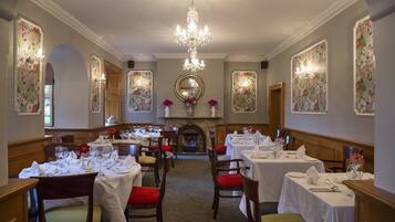 A dining area with multiple tables set for service, a central fireplace, and floral wallpaper.