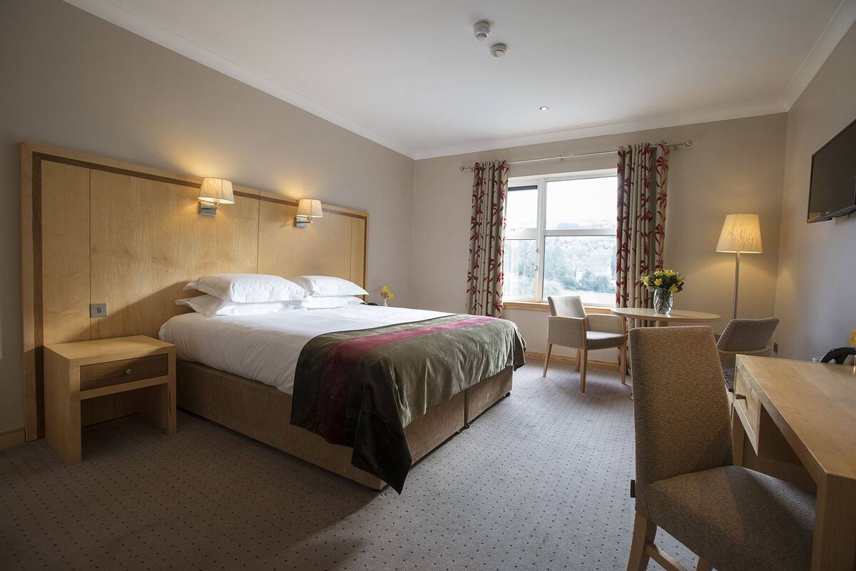 A hotel room with a bed, bedside tables, a desk, and a chair.