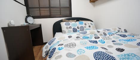 A bedroom with a bed, a nightstand, a wall clock, and a window with blinds.