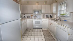 Une cuisine de taille réduite avec des meubles blancs, un four à micro-ondes, une cuisinière et un évier.