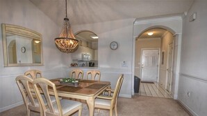 Une salle à manger avec une table et des chaises en bois, un lustre et une cuisine en arrière-plan.