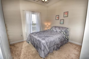 Un dormitorio con cama, ventana con cortinas, lámpara y cuadros en la pared.