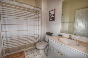 Un baño con cortina de ducha a rayas, un inodoro, un lavabo con espejo y un cuadro en la pared.
