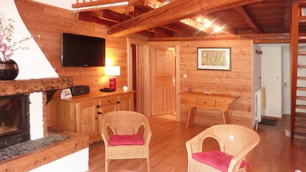 Een gezellig interieur van een blokhut met een open haard, rieten stoelen, een eettafel en een aan de muur bevestigde televisie.