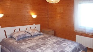Een kamer met houten lambrisering, een bed, twee wandlampen en een raam met dunne gordijnen.
